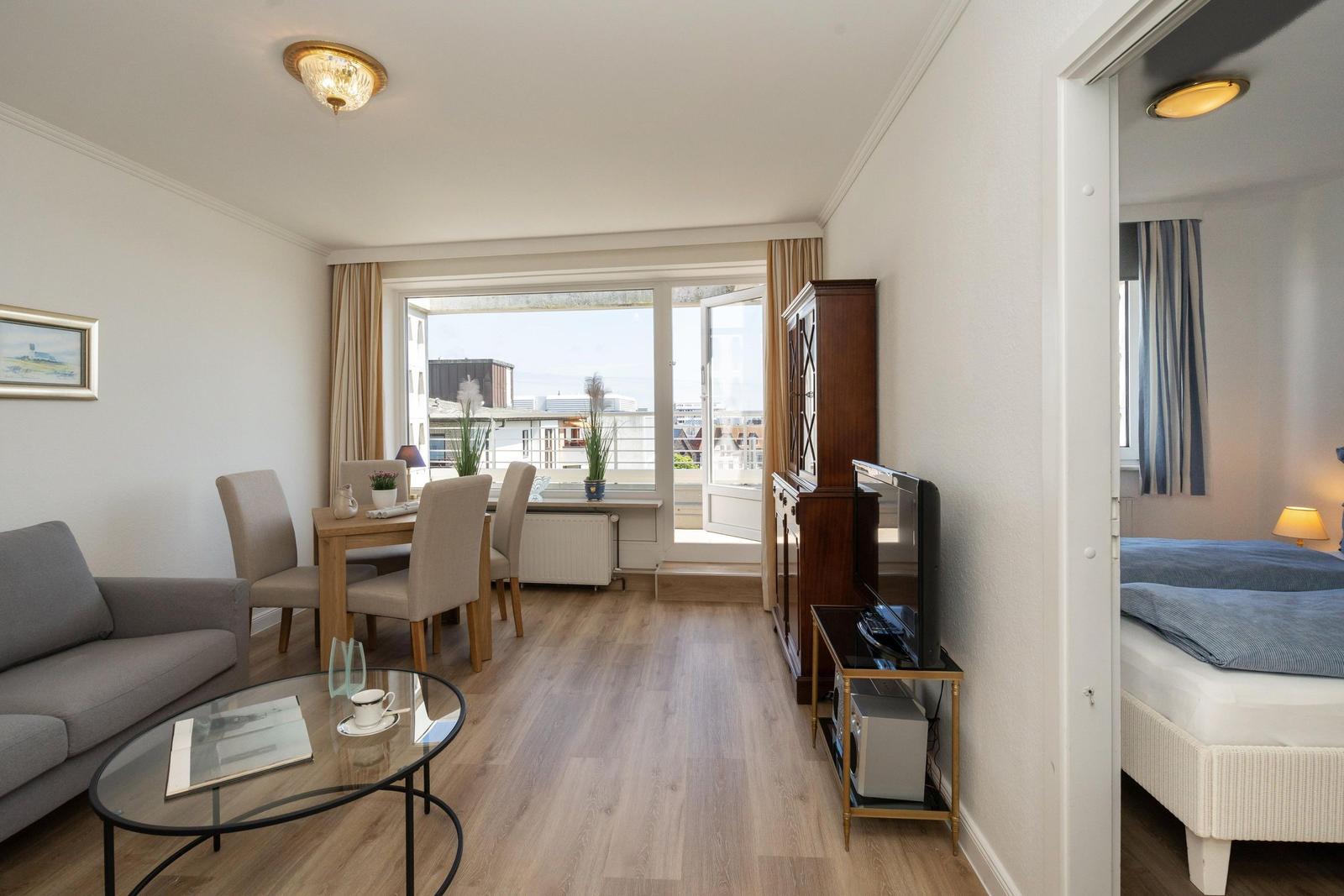 Wohnung mit Essbereich, Balkon und Schlafzimmer. Holzboden und Möbel sichtbar.