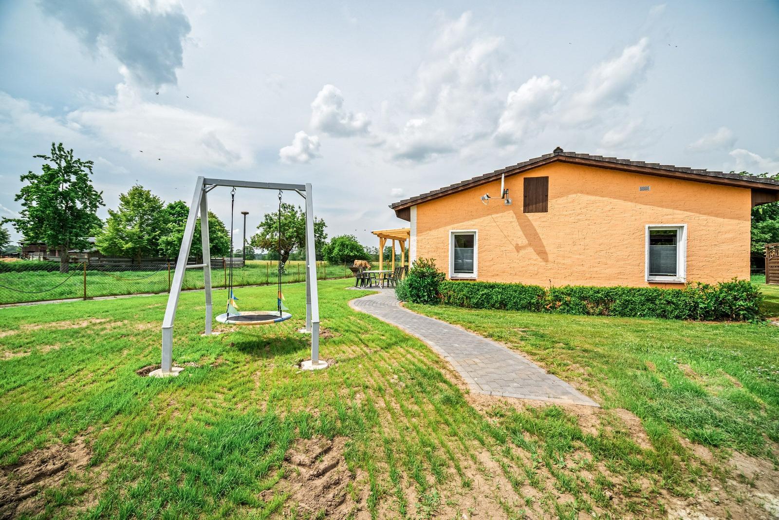 Ein gelbes Haus mit Garten, Spielplatz und Terrasse.
