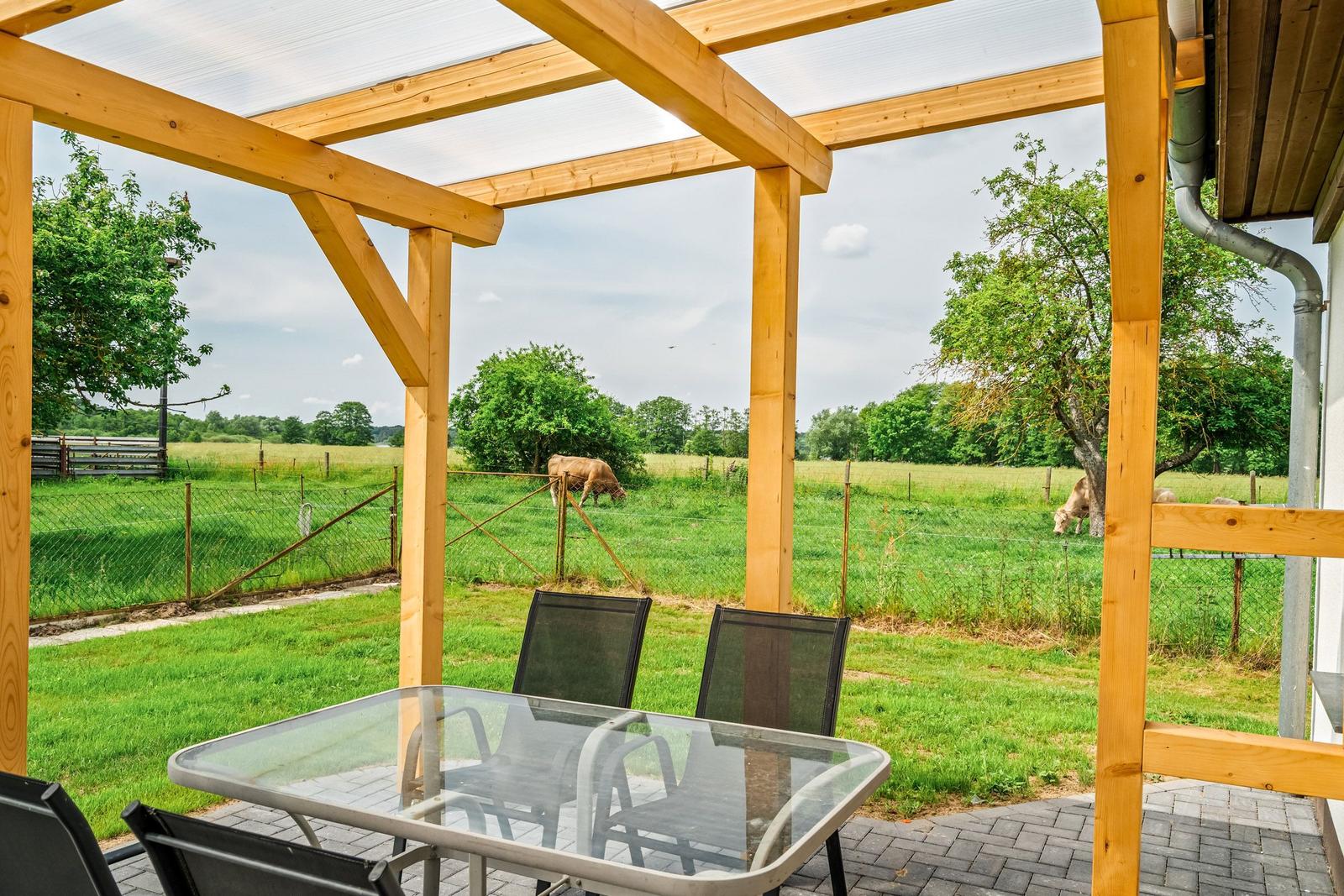 Terrasse mit Glas-Tisch und Stühlen, Blick auf grünes Feld mit Kühen.