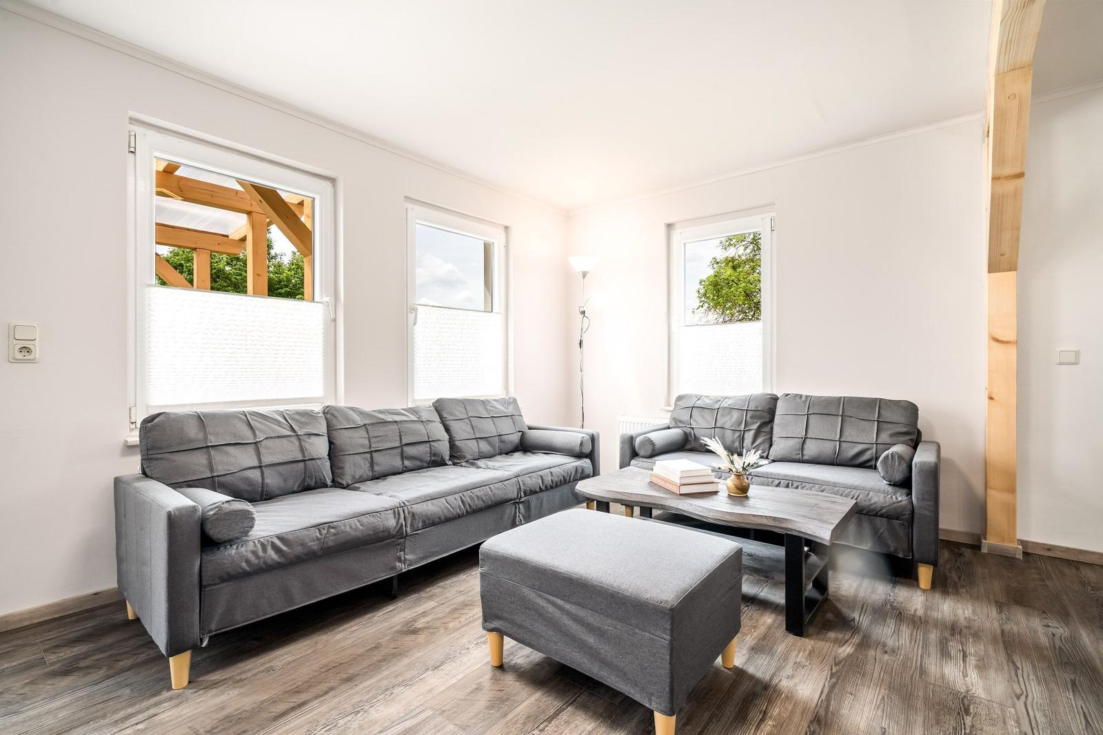 Wohnzimmer mit zwei grauen Sofas, Tisch und Fenstern.