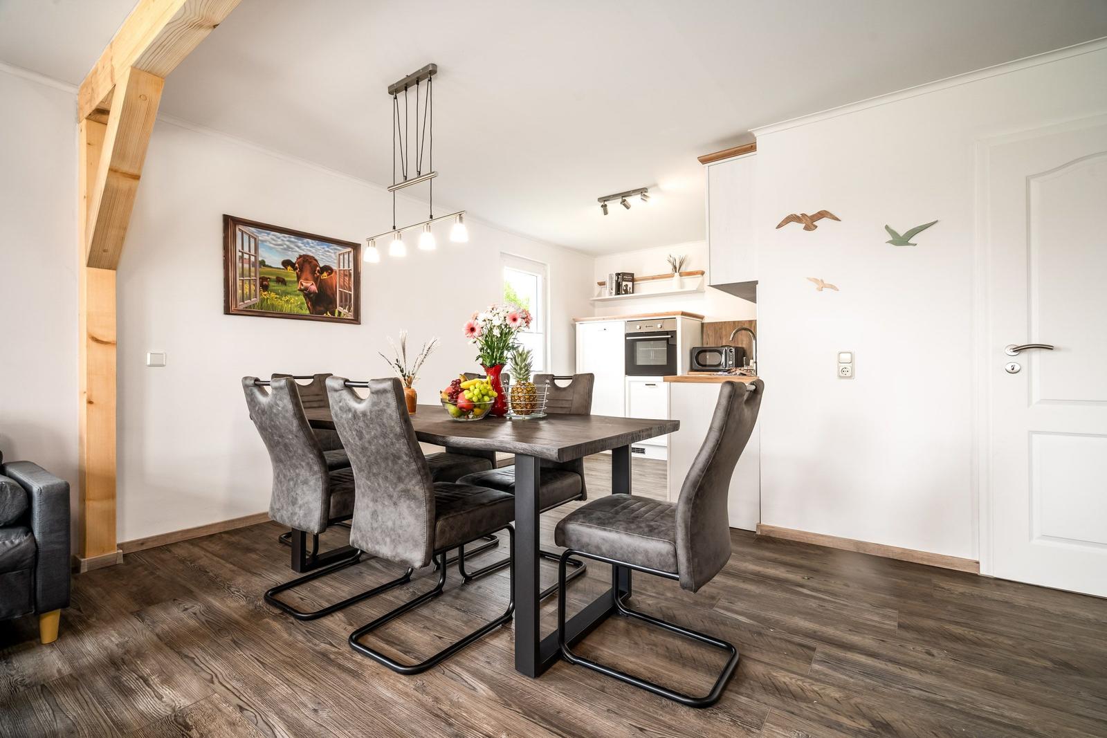 Esszimmer mit Tisch, Stühlen und Küchenbereich. Holzfußboden und Wanddekoration.