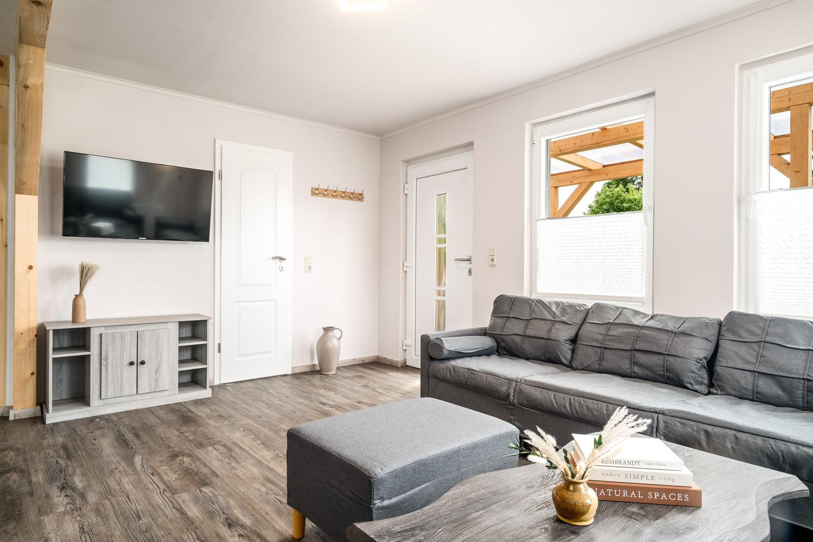 Wohnzimmer mit grauem Sofa, Fernseher und Holzboden.