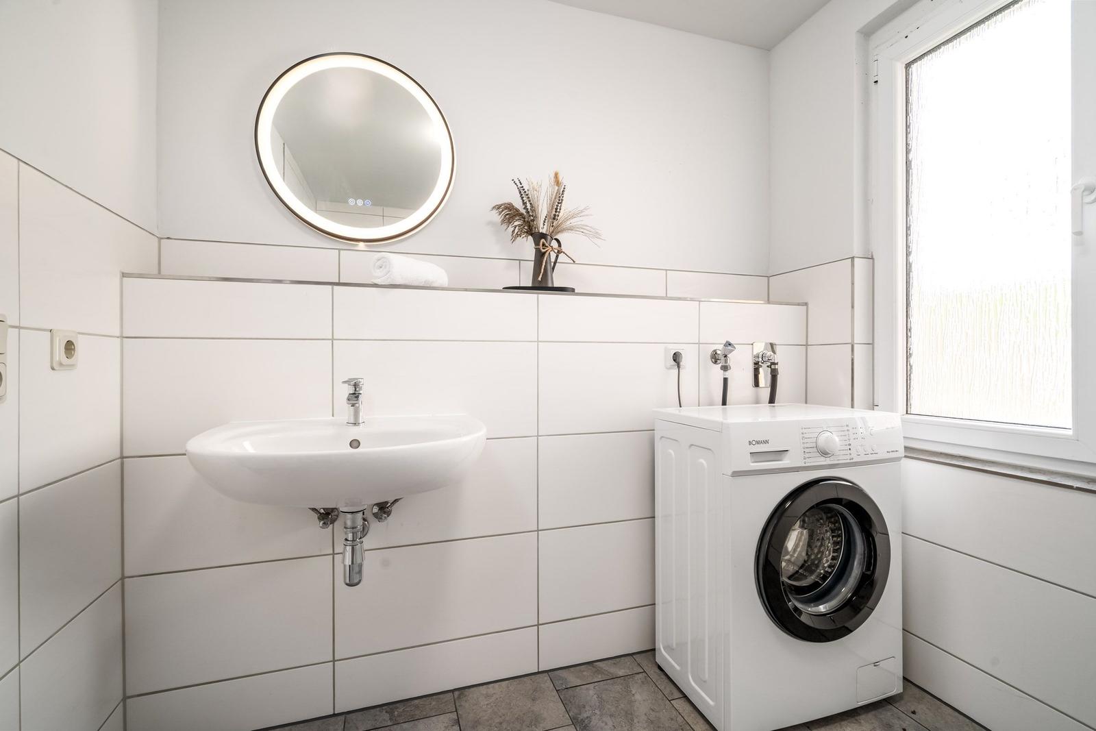 Waschraum mit Waschmaschine, Waschbecken und runden Spiegel an der Wand.