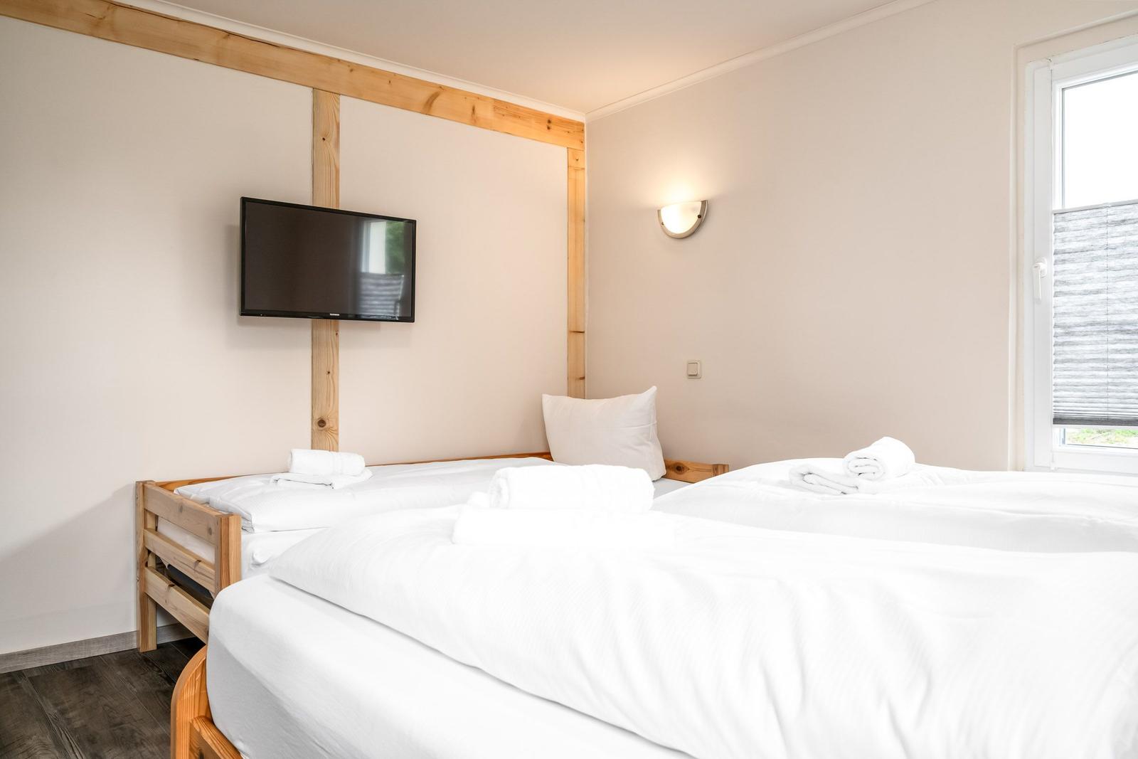 Zwei Betten mit weißen Bettwäschen, Wand-TV und Fenster mit Jalousie.