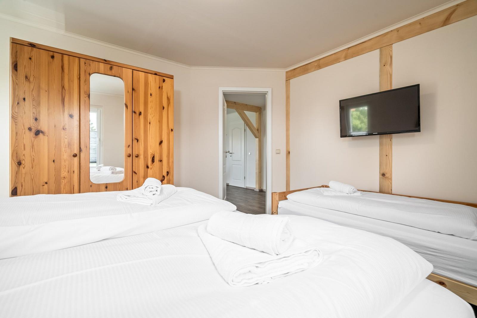 Zwei Betten mit weißen Laken, Holzmöbel und Fernseher an der Wand.