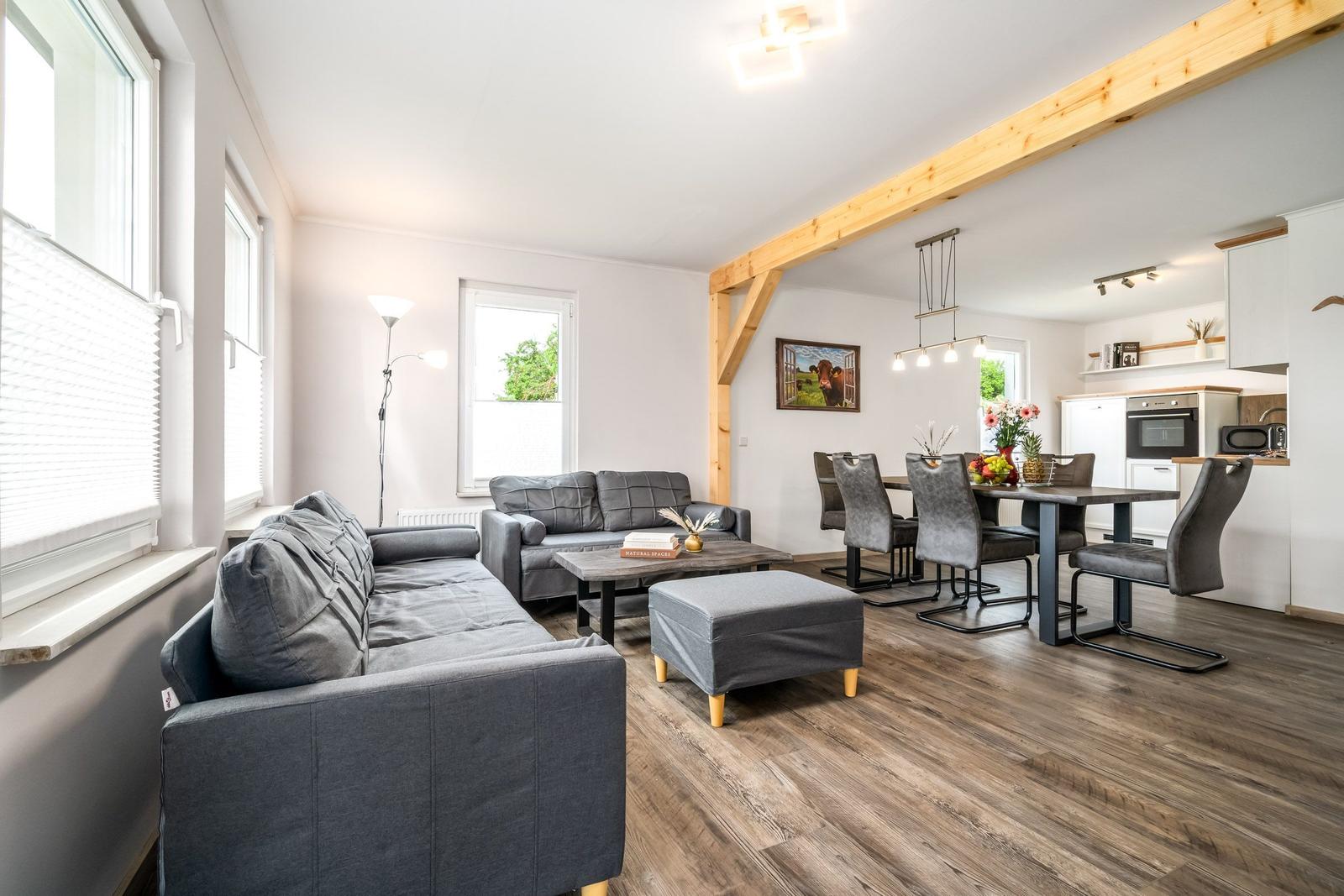 Wohn- und Essbereich mit grauen Sofas, Holzboden und Essgruppe.
