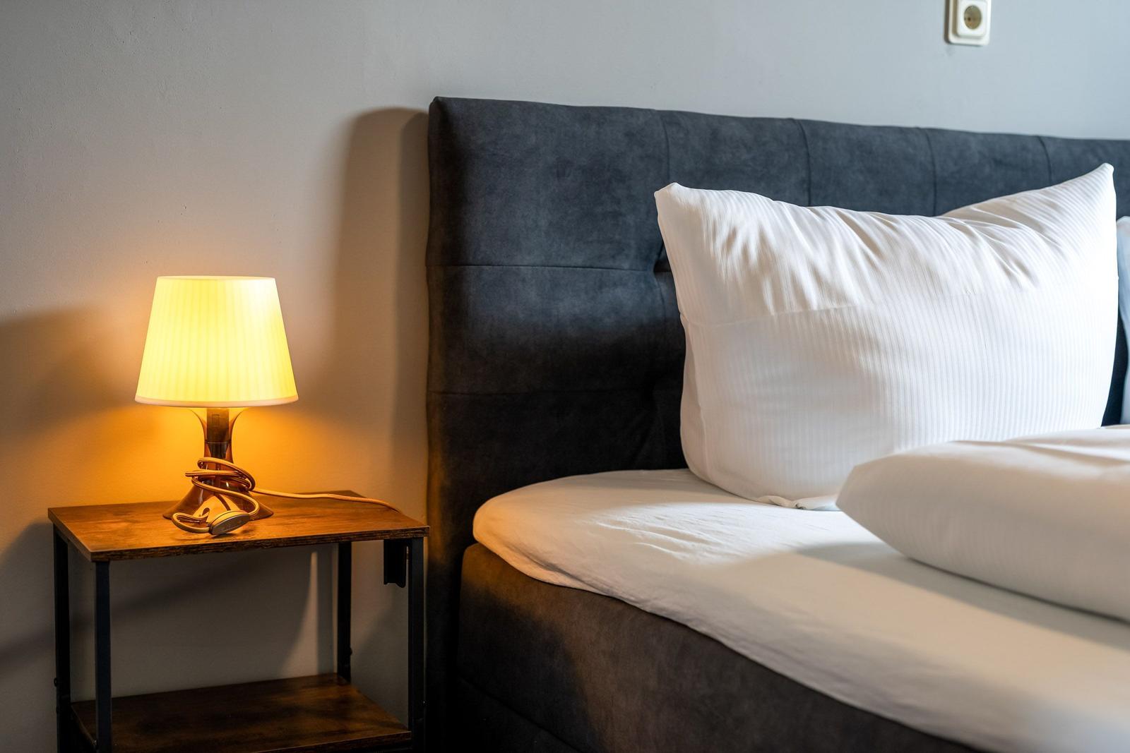 Doppelbett mit dunklem Kopfteil und Nachttisch mit Lampe.