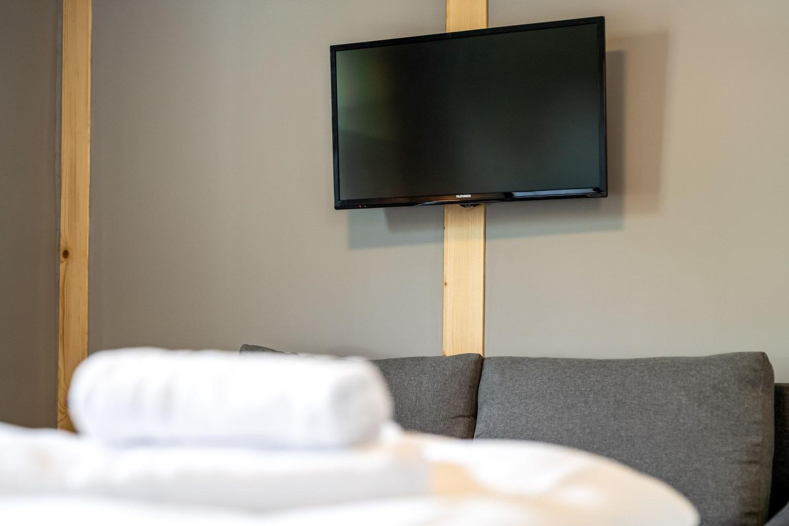 TV an der Wand über einem grauen Sofa mit weißem Handtuch im Vordergrund.