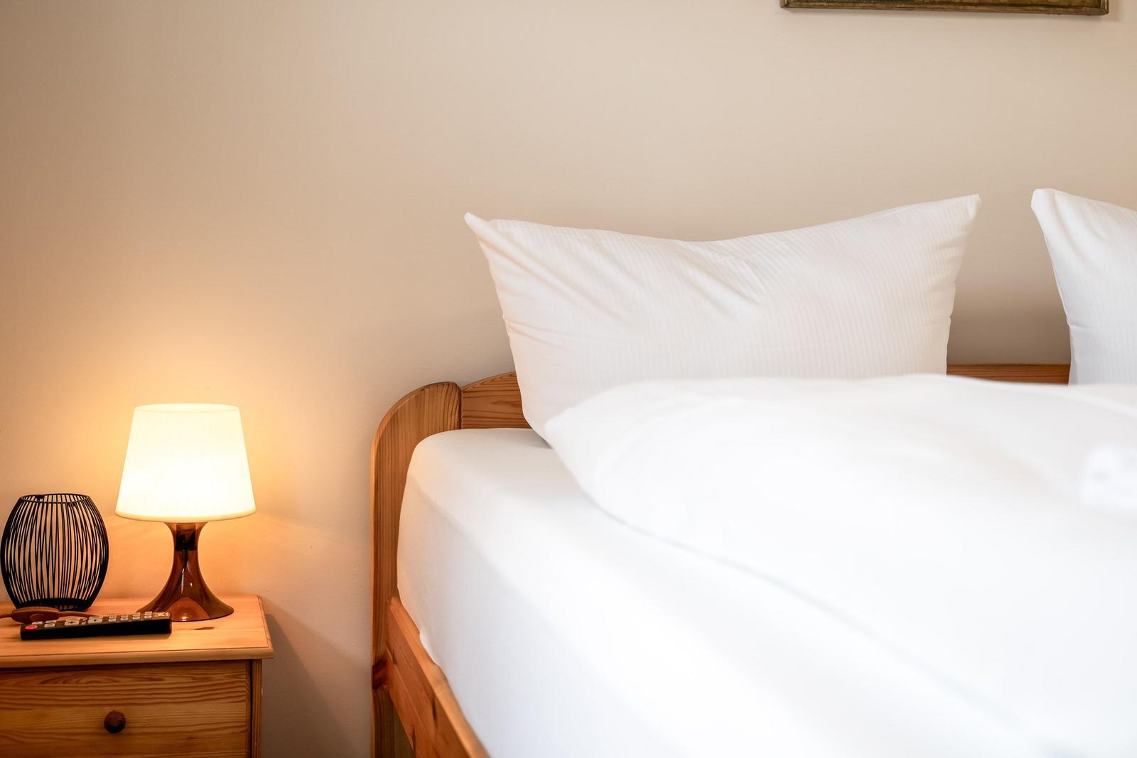 Ein Bett mit weißen Kissen und Bettwäsche neben einem Nachttisch mit Lampe.