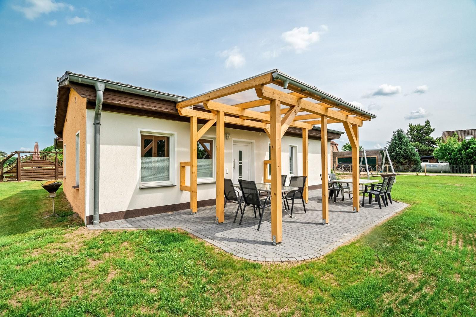 Haus mit Holzveranda, Sitzgelegenheiten und Grillplatz im Garten.