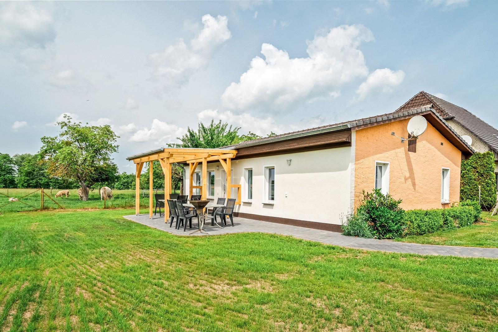 Haus mit Terrasse, Grill und Garten. Im Hintergrund Grasland und Bäume.
