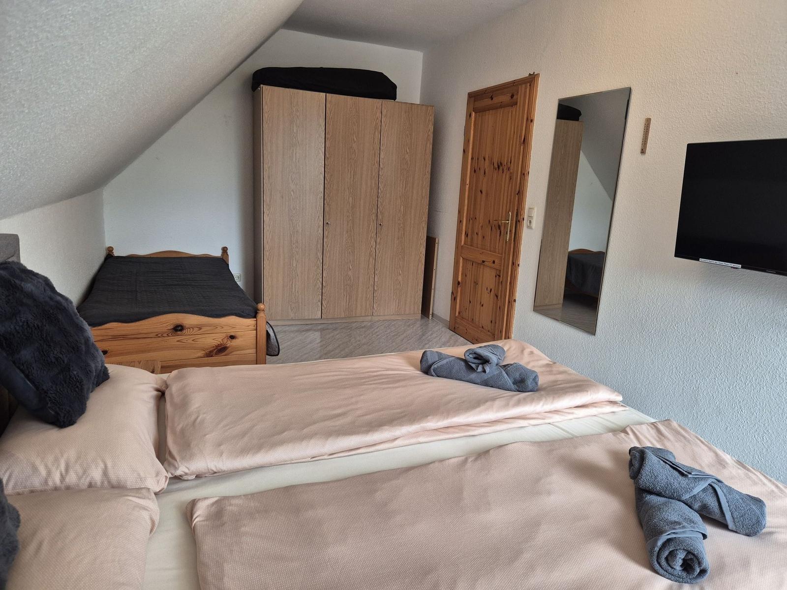 Schlafzimmer mit Doppelbett, Kleiderschrank, Spiegel und Fernseher an der Wand.