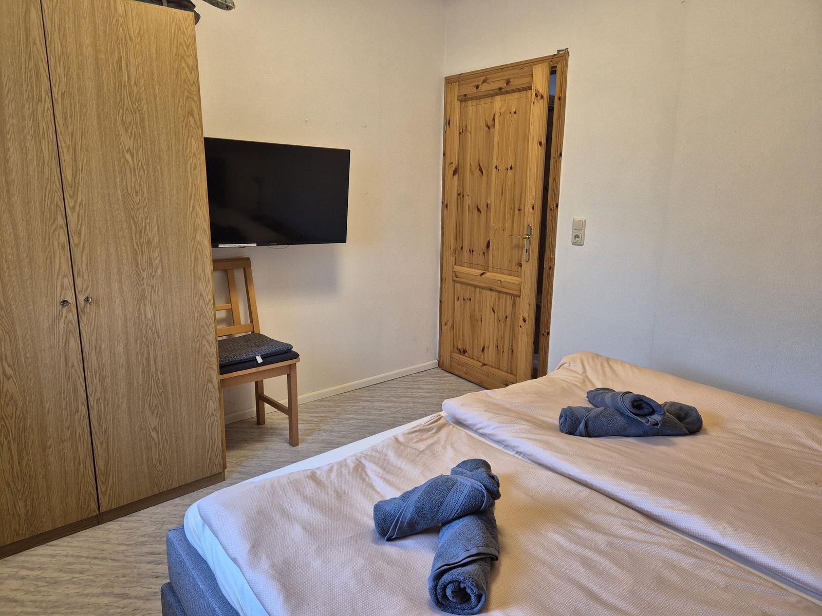 Schlafzimmer mit Doppelbett, Holzschrank, Fernseher und Holztür.