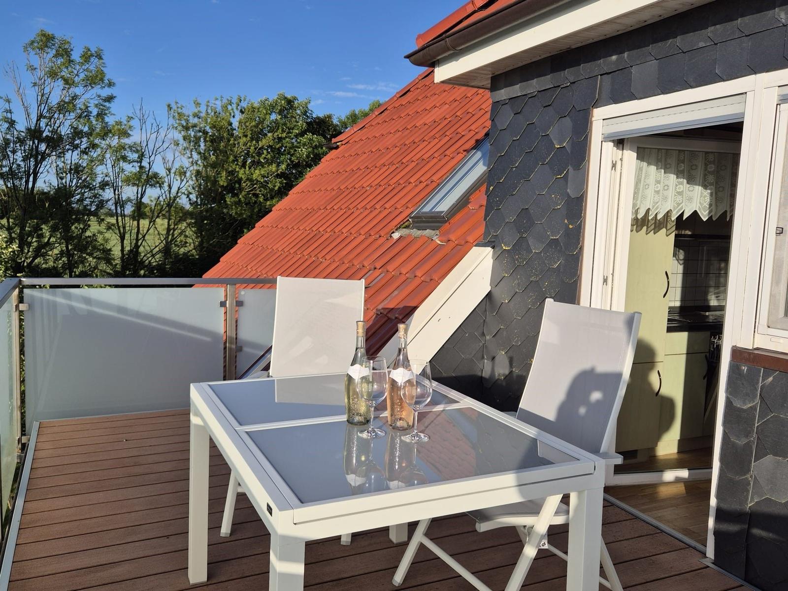 Terrasse mit Tisch und Stühlen, Blick auf Dach und Wald.
