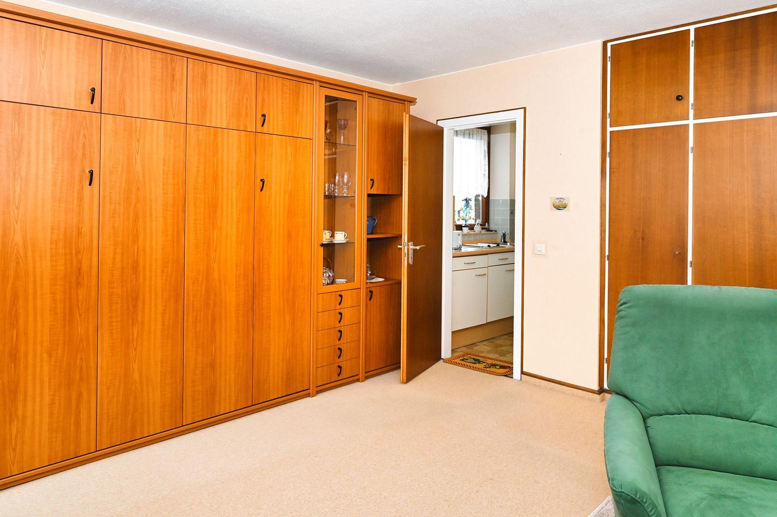 Wohnraum mit grünem Sofa, Holzschrank und Blick in die Küche.