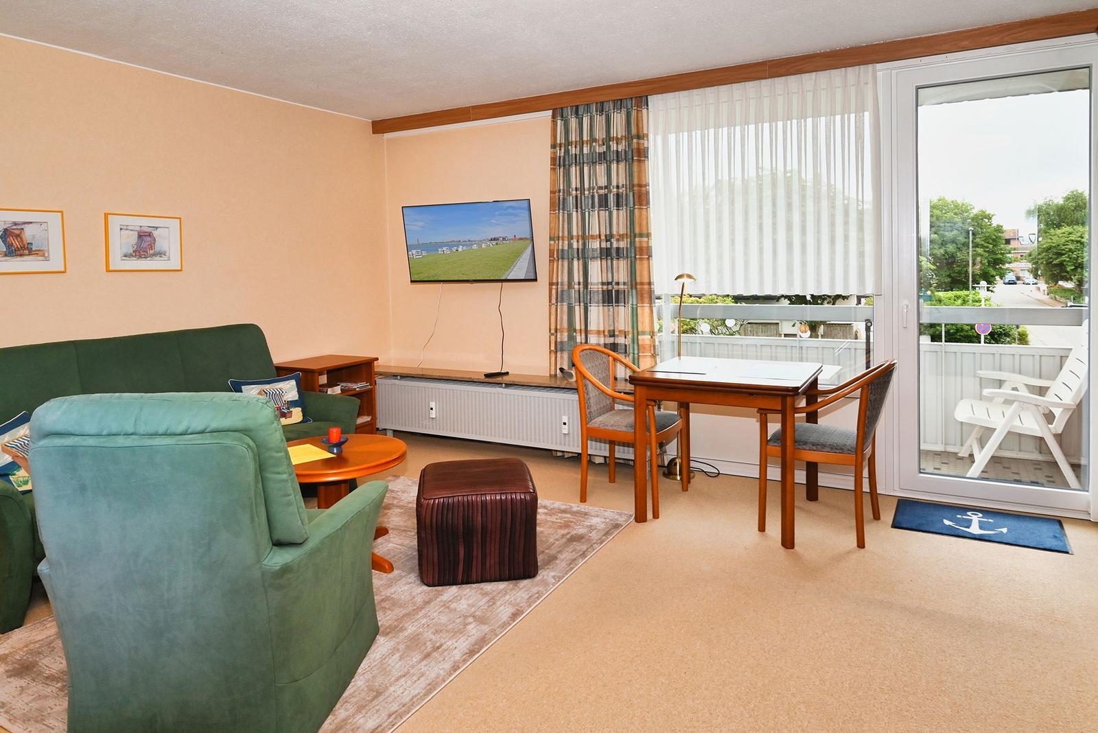 Wohnraum mit Sofa, Sessel, Esstisch und Balkon. Fernseher an der Wand.