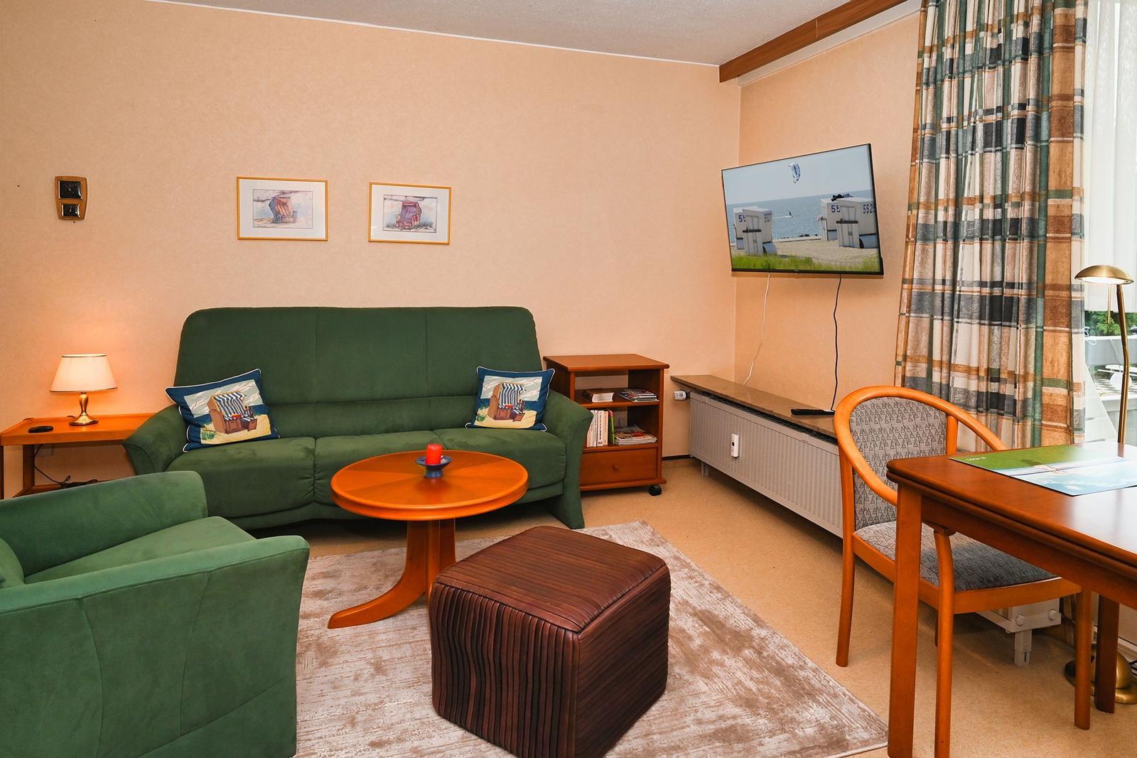 Ein Wohnzimmer mit grünem Sofa, runden Tisch und Fernseher an der Wand.
