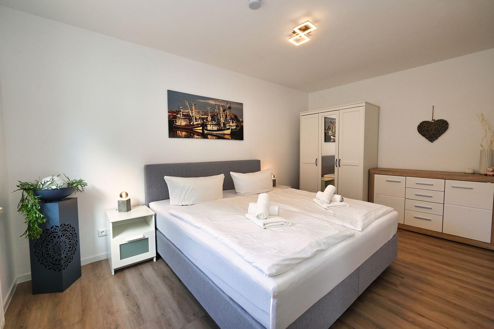 Schlafzimmer mit Doppelbett, Kleiderschrank und Nachttisch. Wandbild und Holzboden.