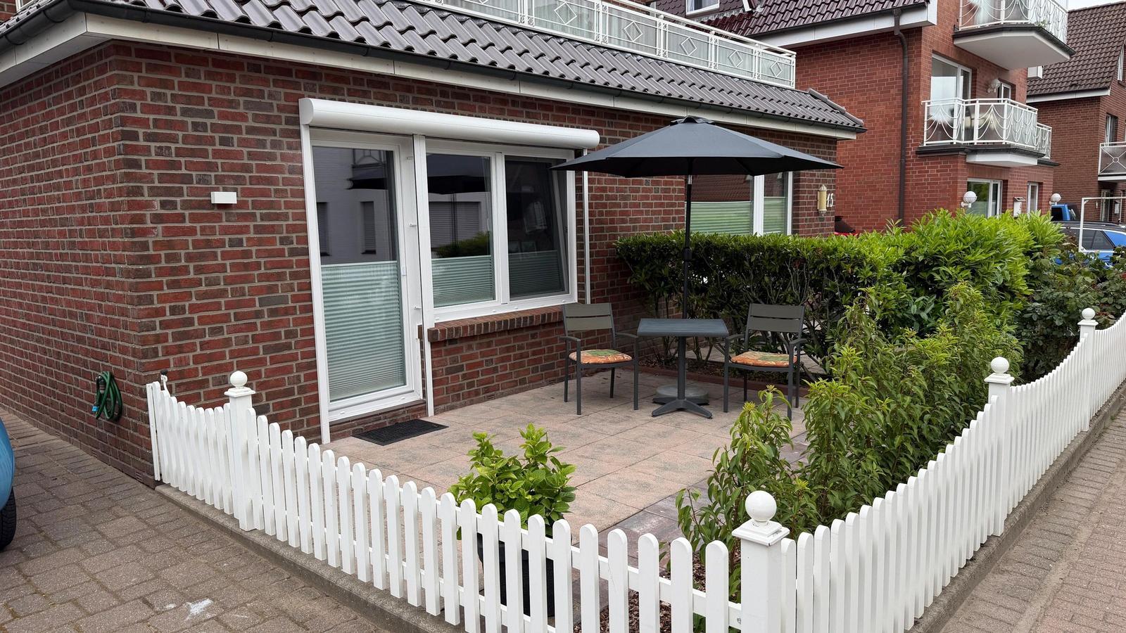 Terrasse mit Tisch, Stühlen und Sonnenschutz vor einem roten Backsteinhaus.