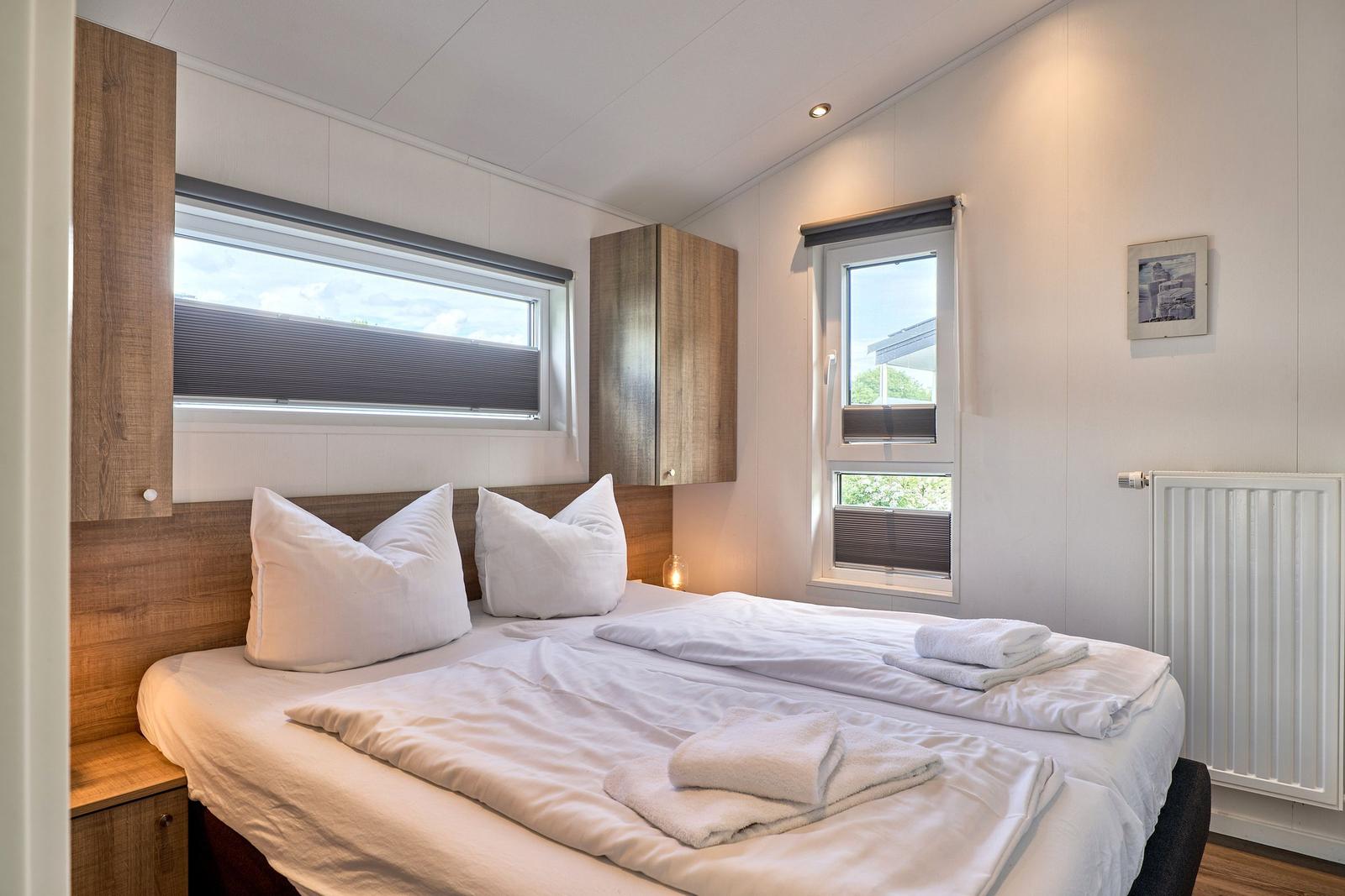 Schlafzimmer mit Doppelbett, zwei Fenstern und Holzmöbeln.
