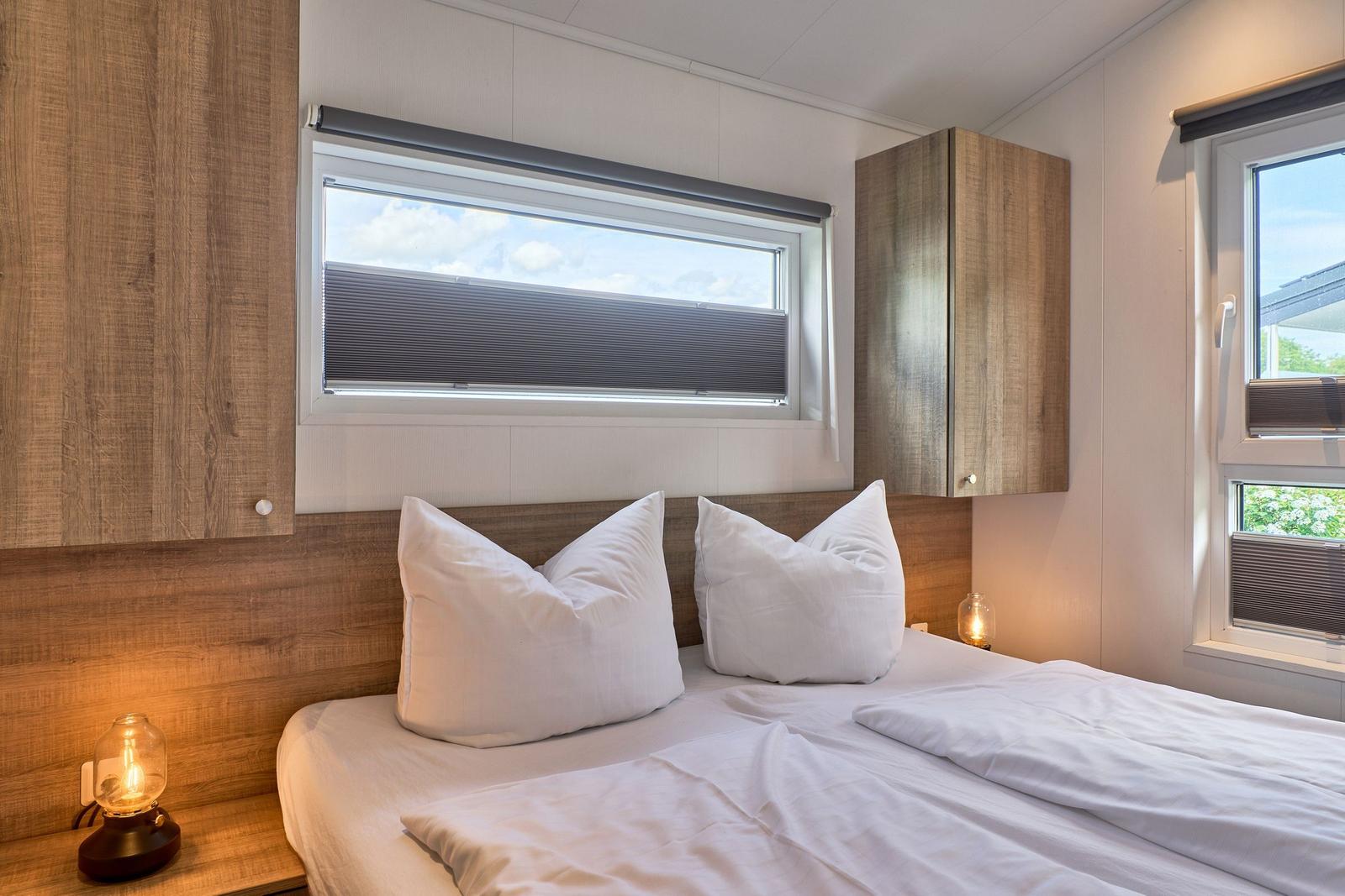 Schlafzimmer mit Doppelbett, zwei Fenstern und Holzregalen an den Wänden.
