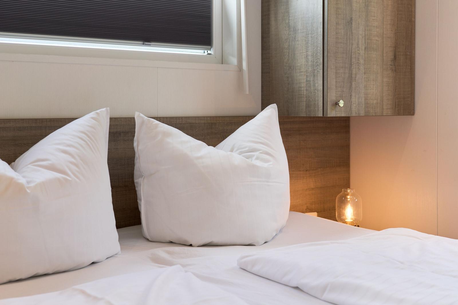 Ein Bett mit weißen Kissen und einer Bettdecke. An der Wand hängt ein Schrank.