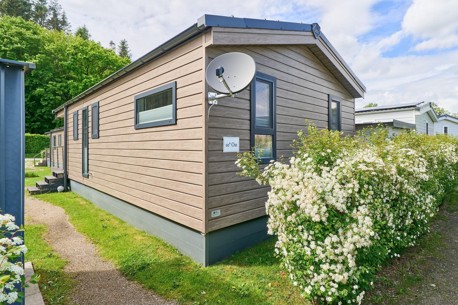 Moderne Ferienwohnung mit Satellitenantenne und Blumenhecke im Grünen.