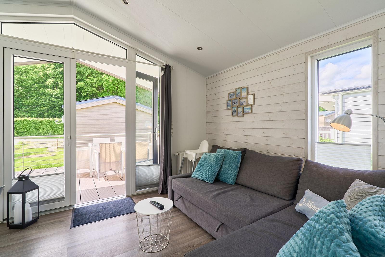 Wohnzimmer mit Sofa, Fenster und Terrasse. Holzwand und moderne Einrichtung.