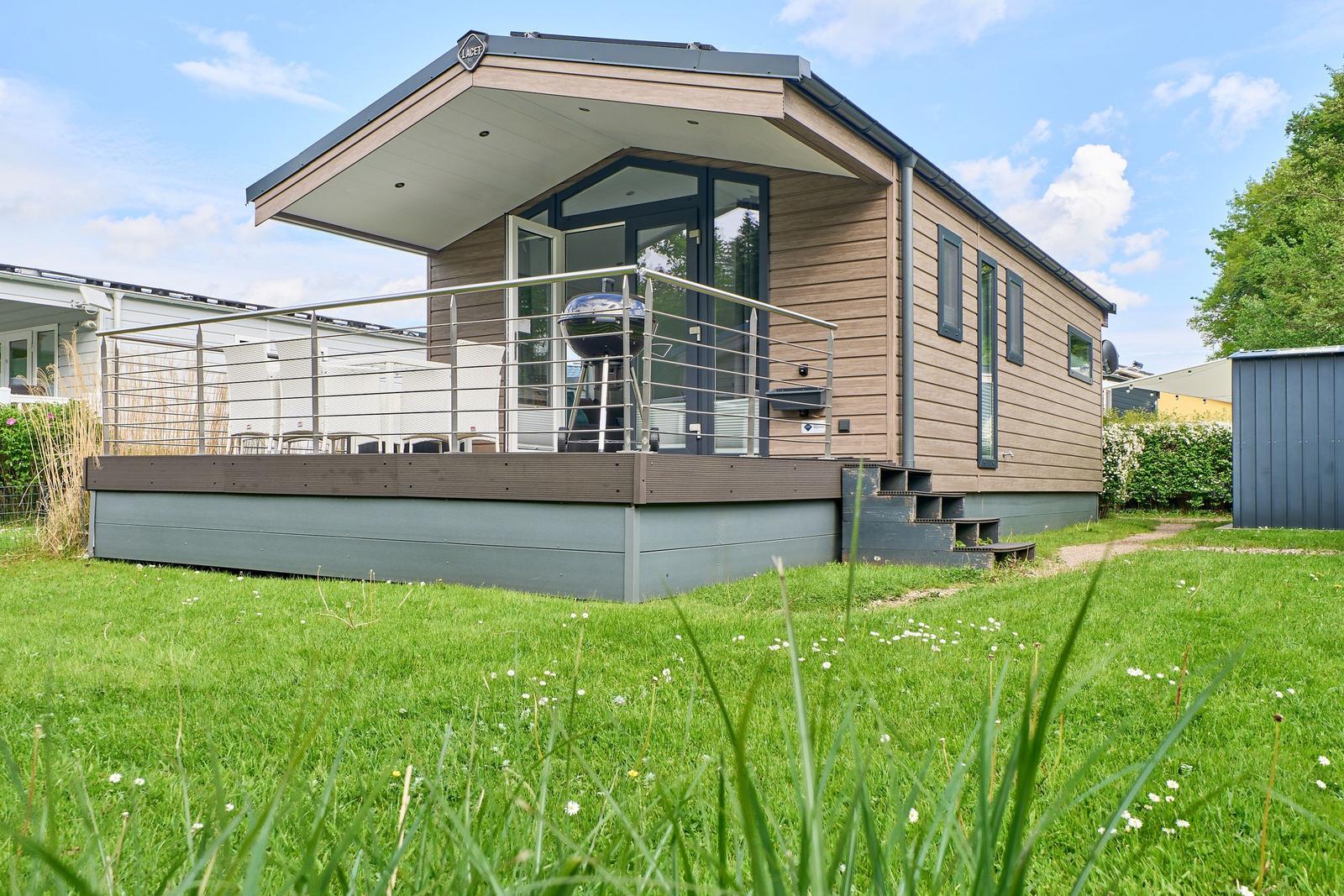 Moderne Ferienhaus mit Terrasse, Grill und grünem Garten.