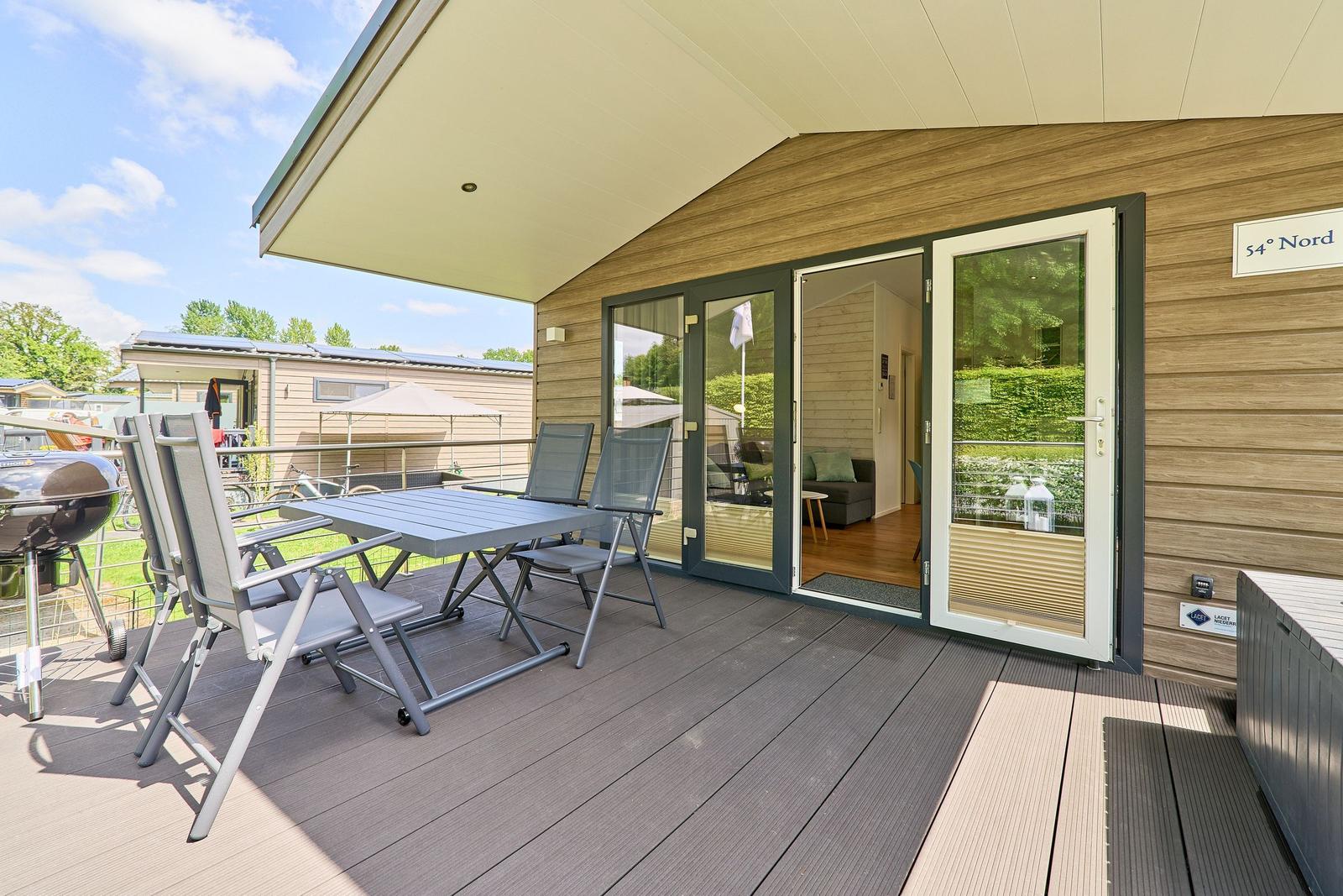 Terrasse mit Tisch, Stühlen und Grill. Durchgehende Glastüren führen ins Innere.