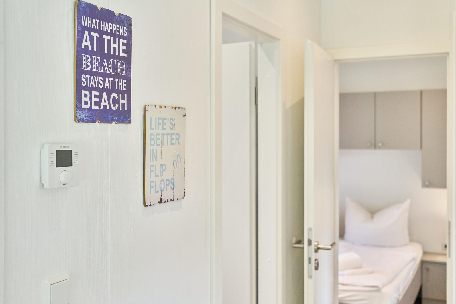 Wand mit Schildern und Blick in Schlafzimmer mit Bett und Schränken.