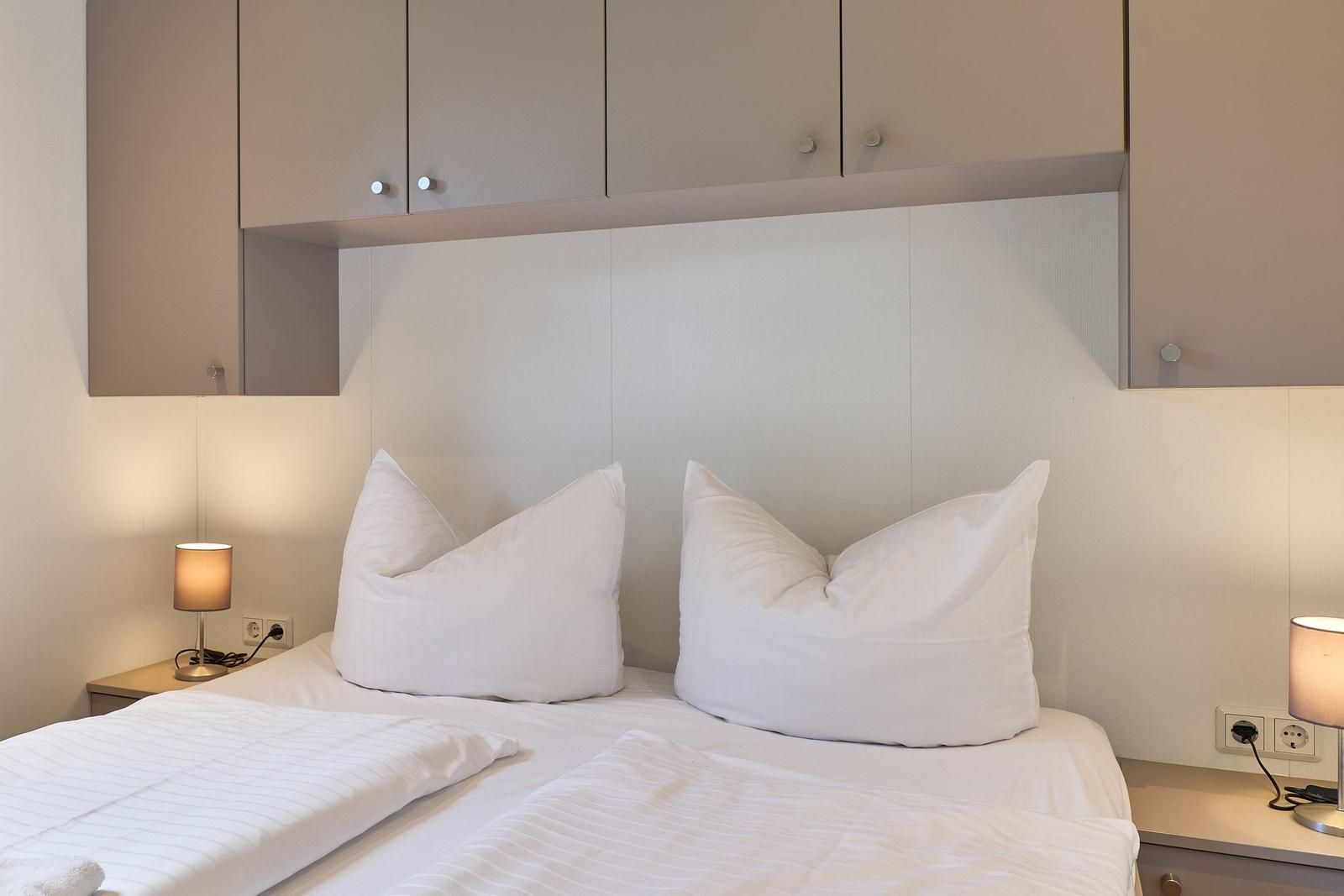 Schlafzimmer mit Bett, zwei Kissen und Nachttischen mit Lampen.