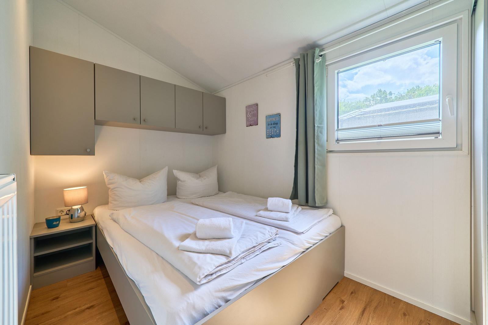Schlafzimmer mit Doppelbett, Nachttisch, Fenster und Schränken.