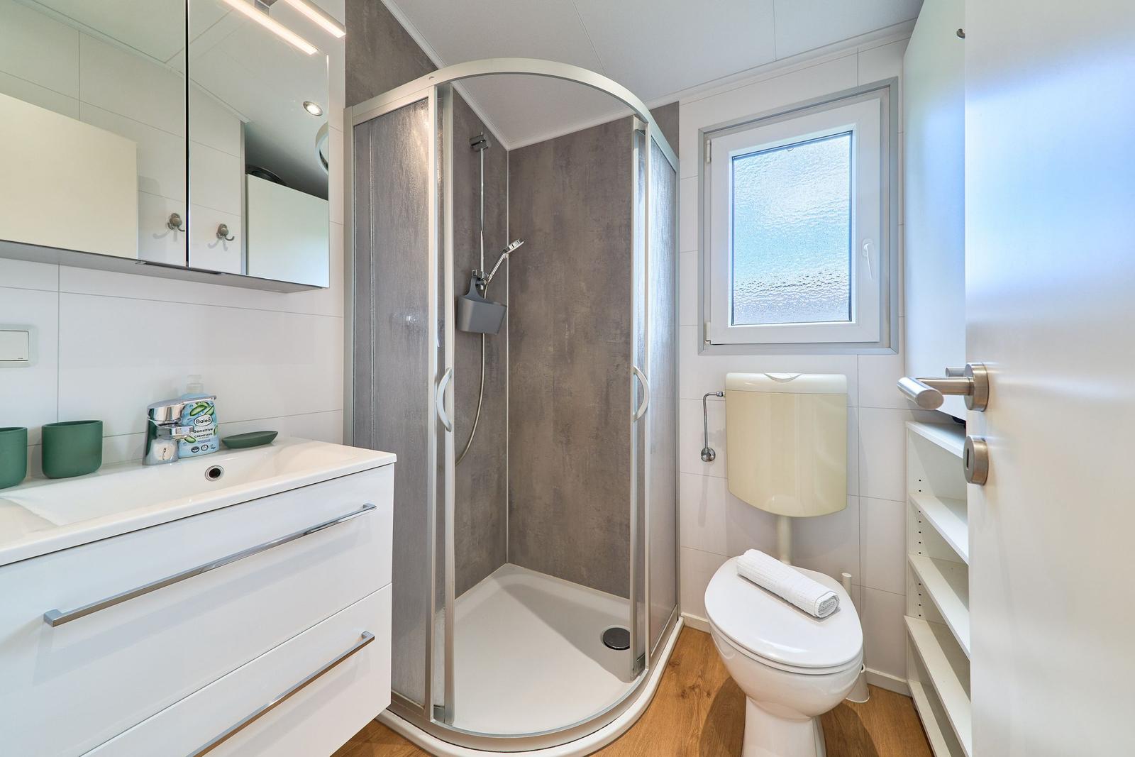 Badezimmer mit Dusche, Waschbecken und Toilette. Fenster mit getöntem Glas.