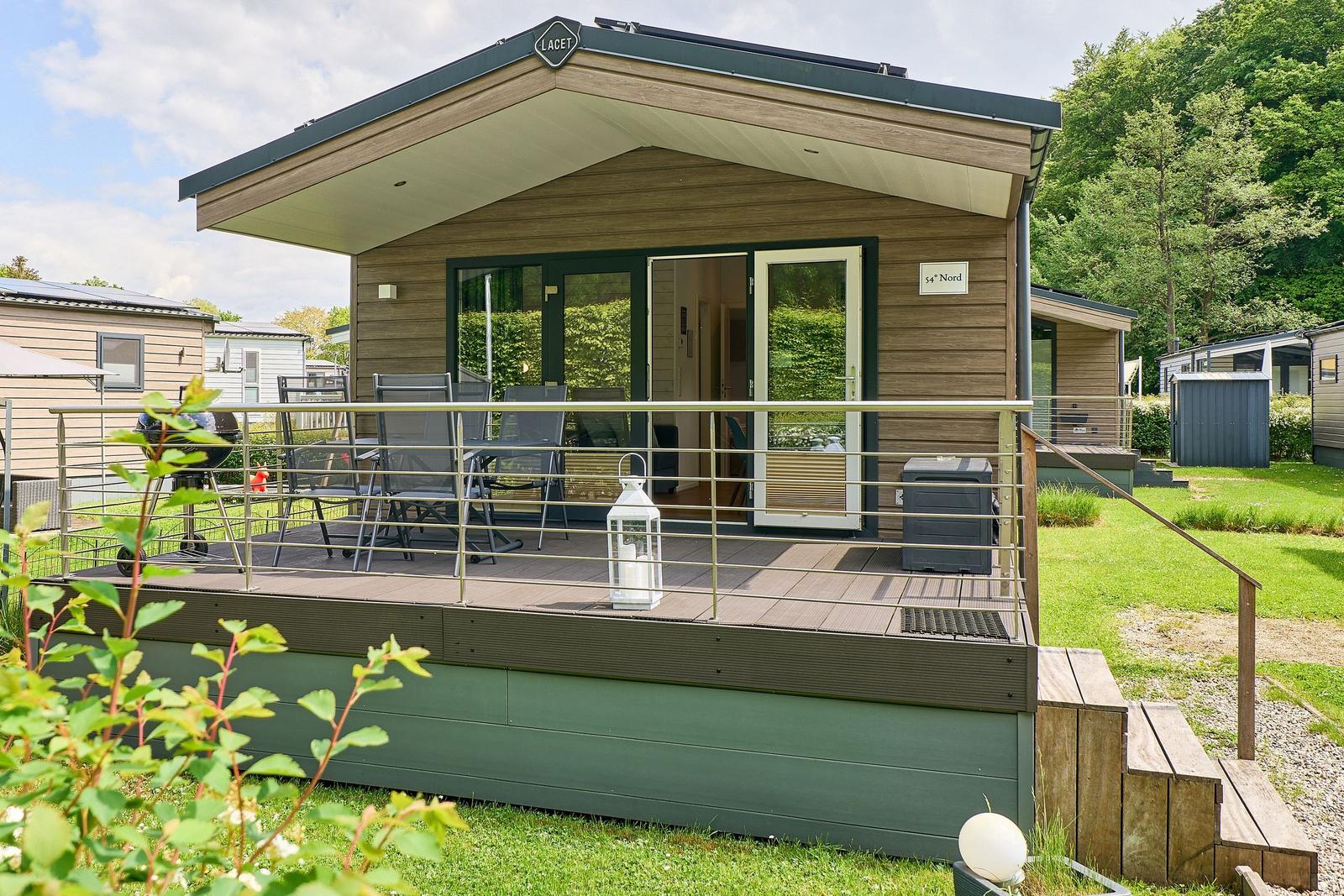 Holzhaus mit Terrasse, Grill und Sitzgelegenheiten im Grünen.