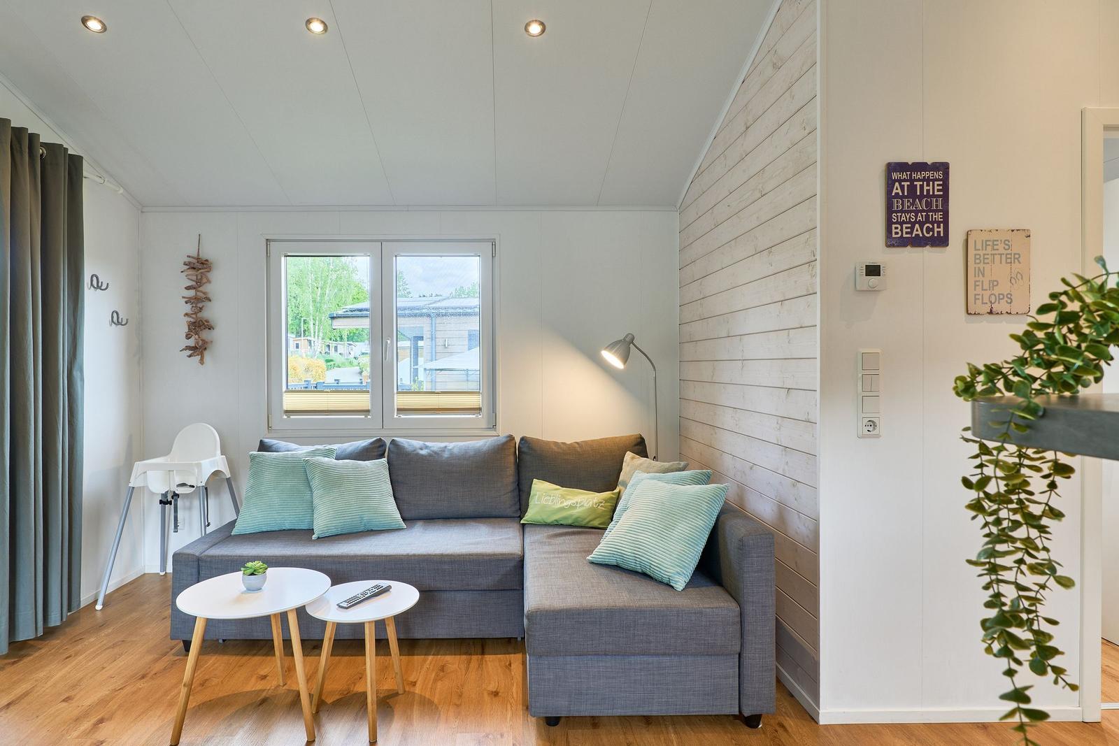 Ein Wohnbereich mit grauem Sofa, zwei runden Tischen und einem Fenster.