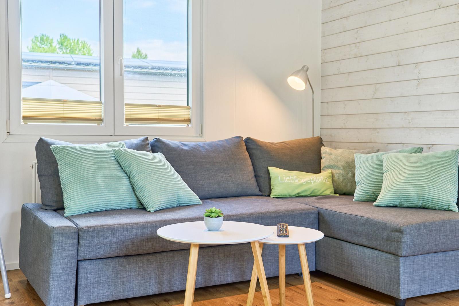 Ein grauer Sofa mit grünen Kissen und einem runden Tisch vor einem Fenster.
