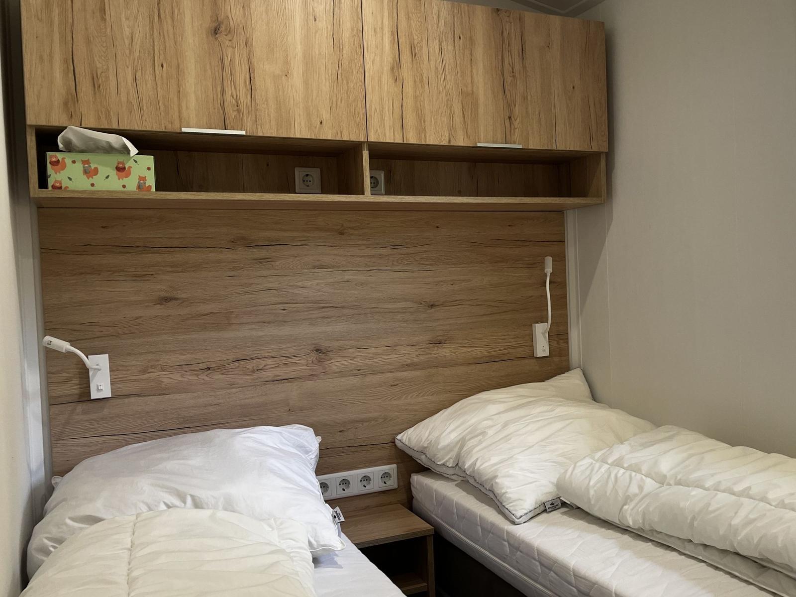 Zwei Betten mit weißen Bettwäschen unter einem Holzregal mit Steckdosen.