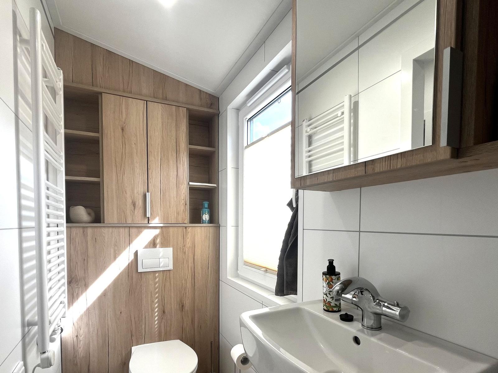 Badezimmer mit Holzschränken, Waschbecken und Fenster.