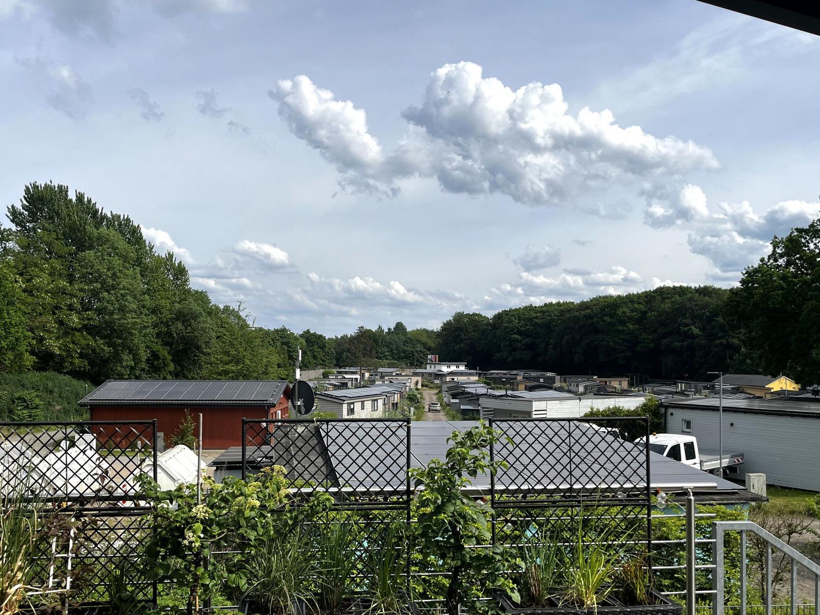 Terrasse mit Blick auf Wohnanlage und Wald unter bewölktem Himmel.