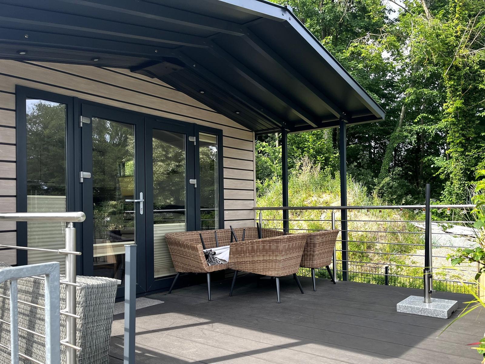Terrasse mit Sitzgruppe unter Markise, umgeben von Wald.