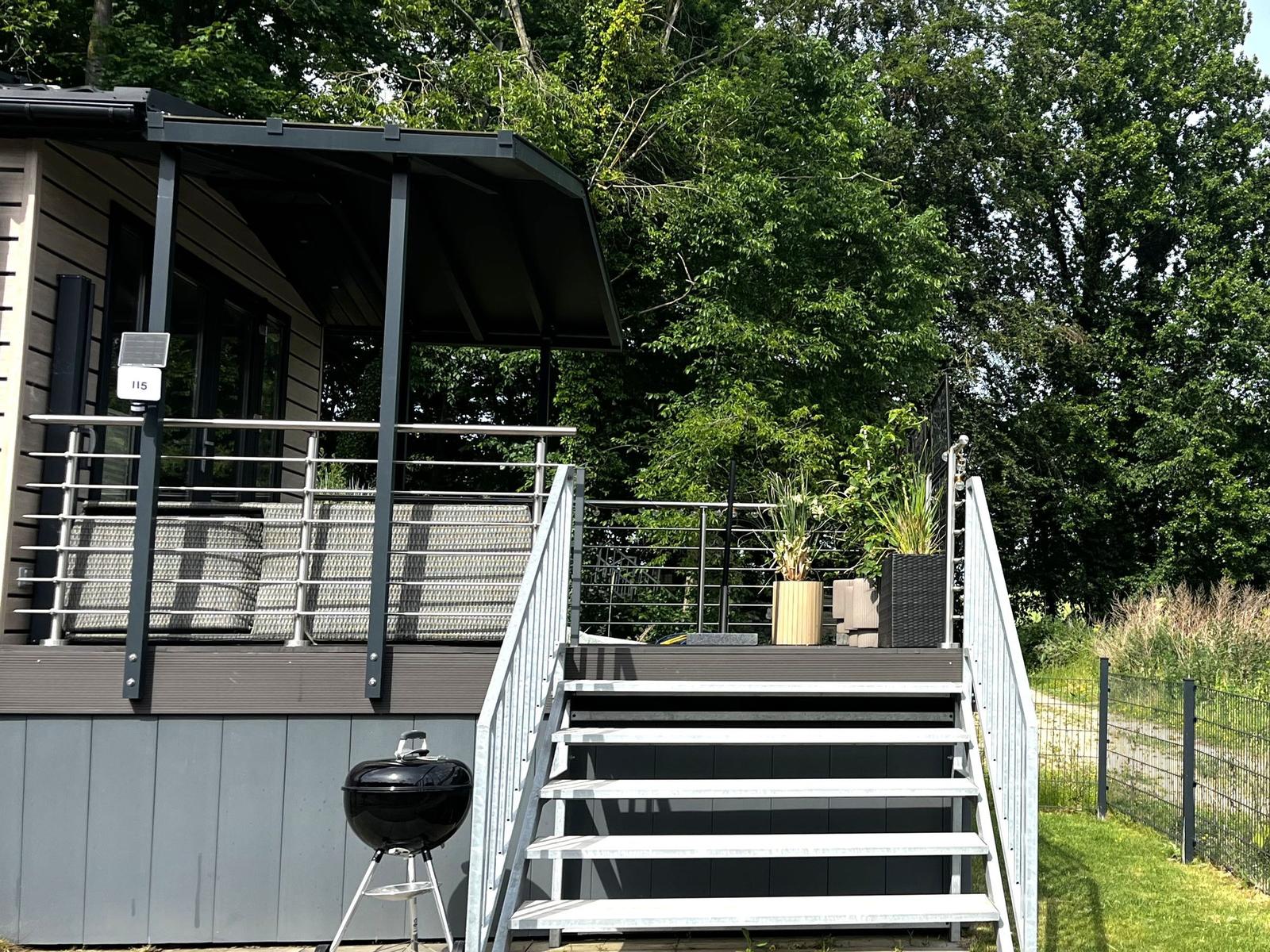 Terrasse mit Stufen, Grill und Pflanzen vor einem Haus mit Balkon.
