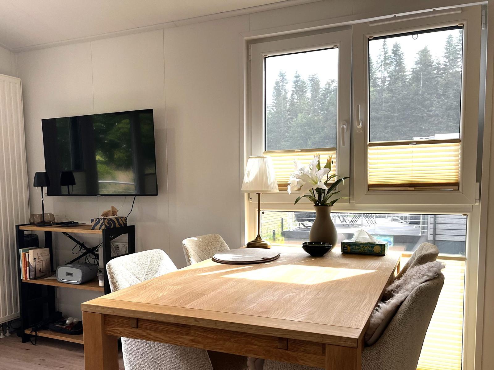 Essbereich mit Holztisch, Stühlen und Fensterblick auf Wald.