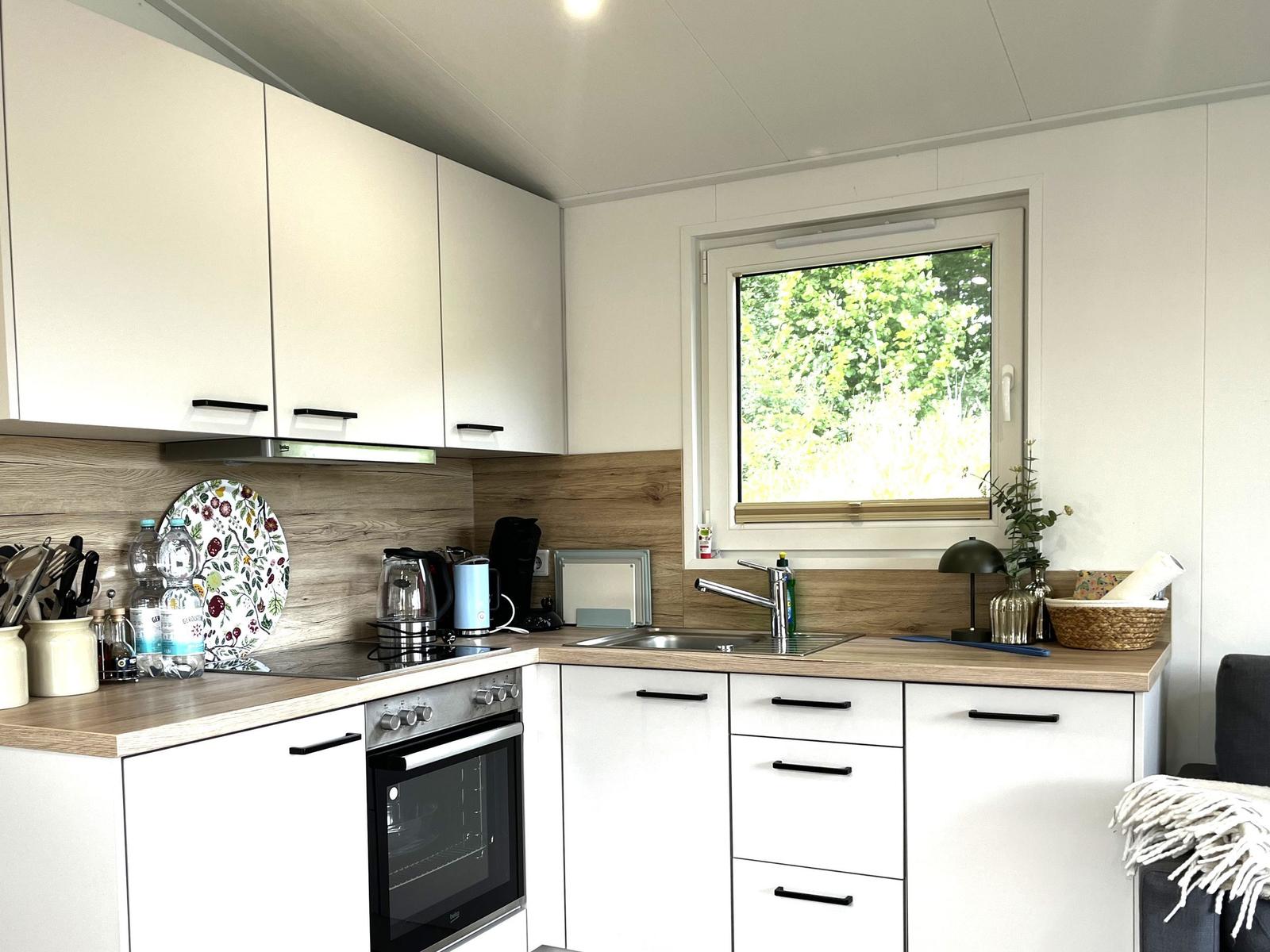 Küche mit weißen Schränken, Holz Arbeitsplatte und Fenster zum Garten.