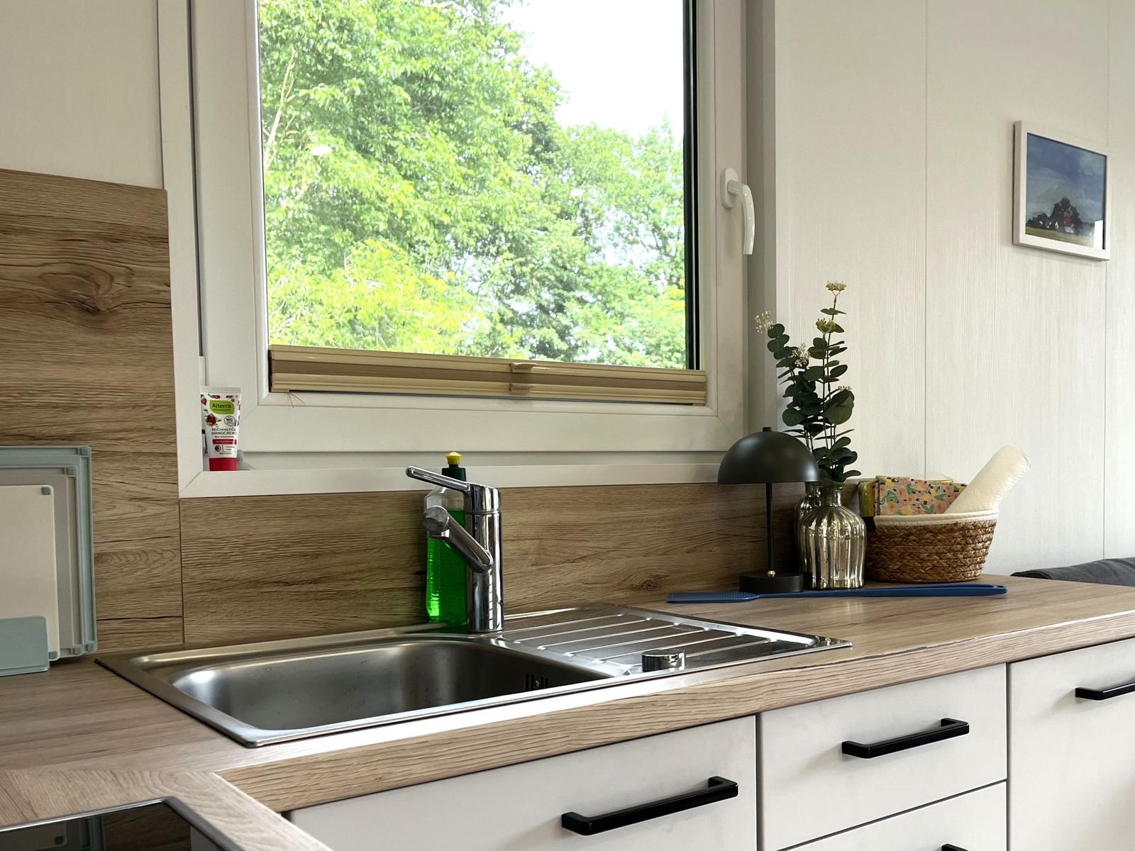 Küchenzeile mit Spüle, Fenster und Pflanze. Holzoptik und weiße Schränke.