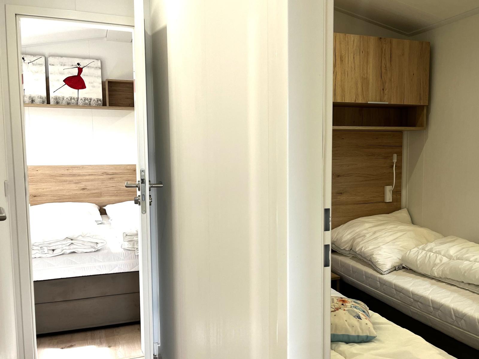 Zimmer mit zwei Betten und Holzmöbeln. Tür führt zu einem Schlafzimmer.
