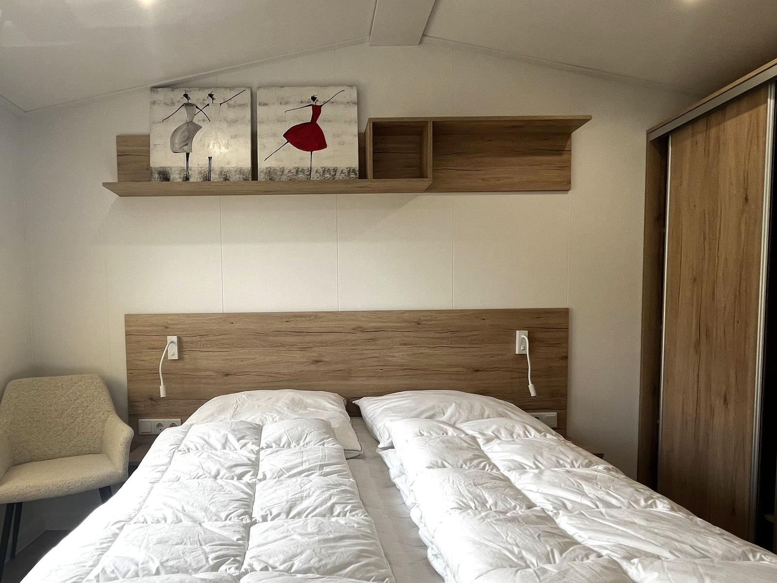 Schlafzimmer mit Doppelbett, Holzkopfteil, Wandregal und Stuhl.