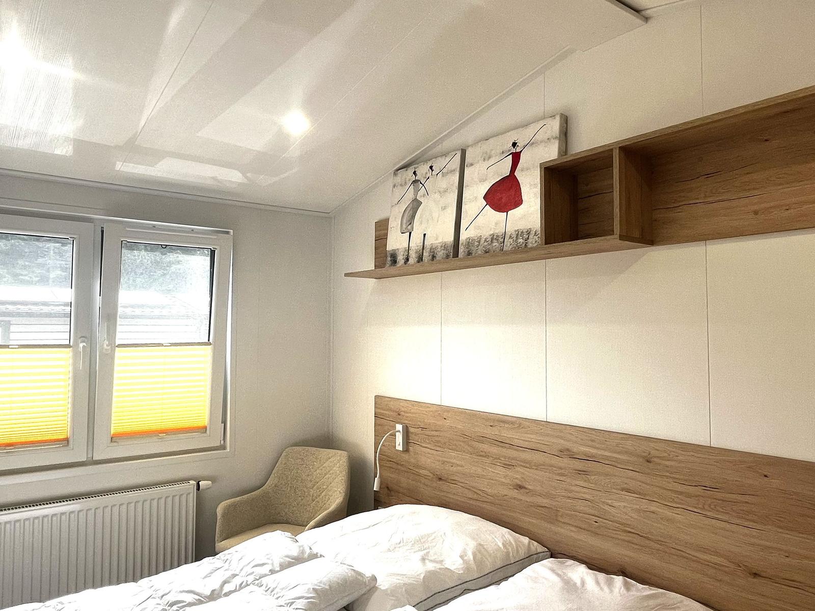 Schlafzimmer mit Bett, Fenster, Stuhl und Wandregal mit Bildern.