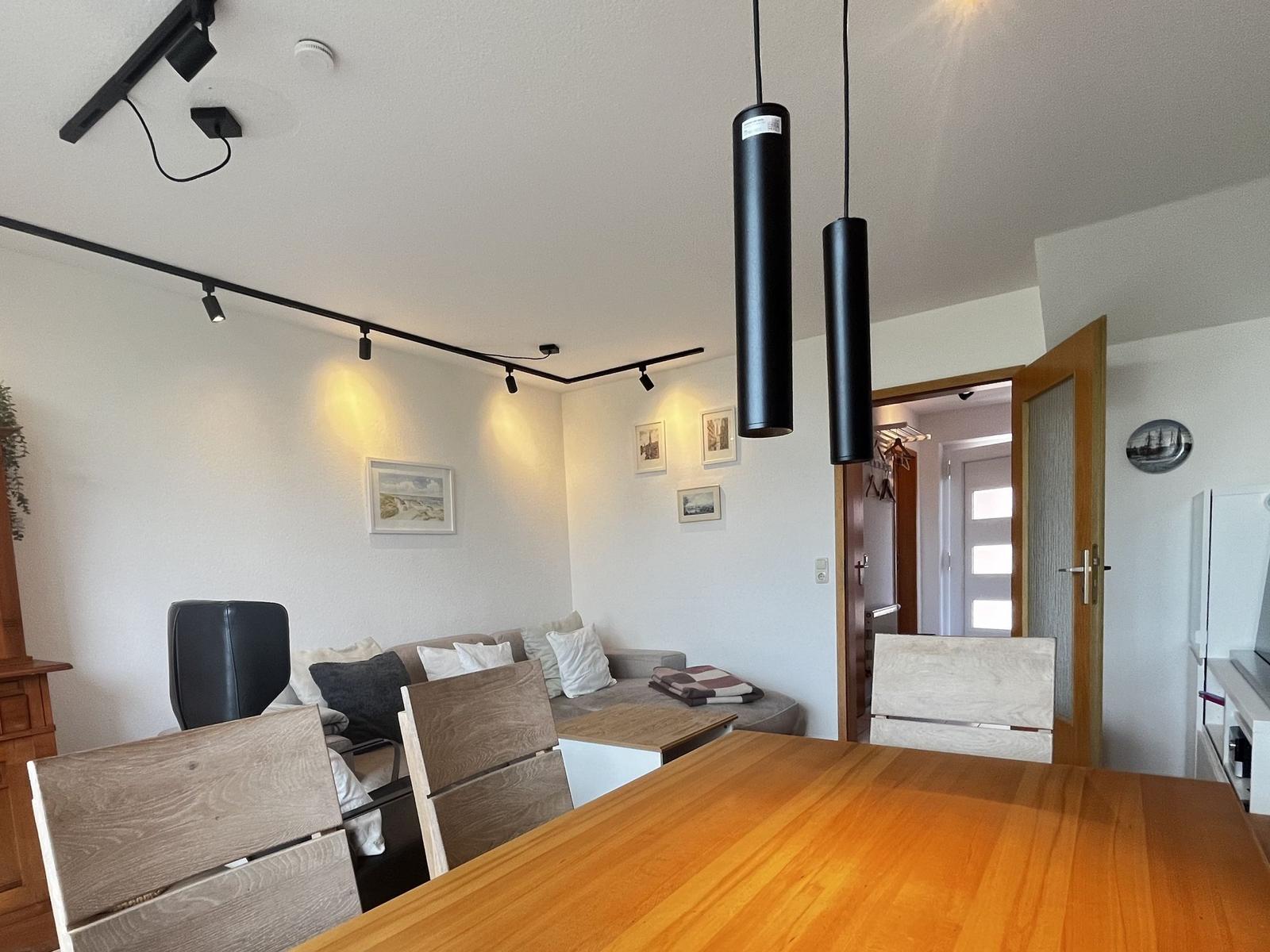 Essbereich mit Holztisch und Stühlen, Wohnbereich mit Sofa und Deckenleuchten.