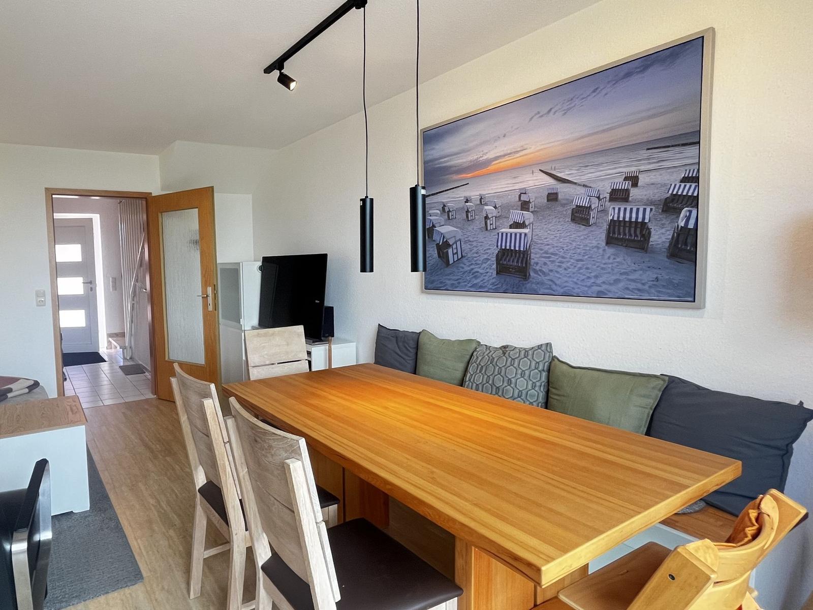 Essbereich mit Holztisch, Stühlen und Wandbild von Strandkörben.